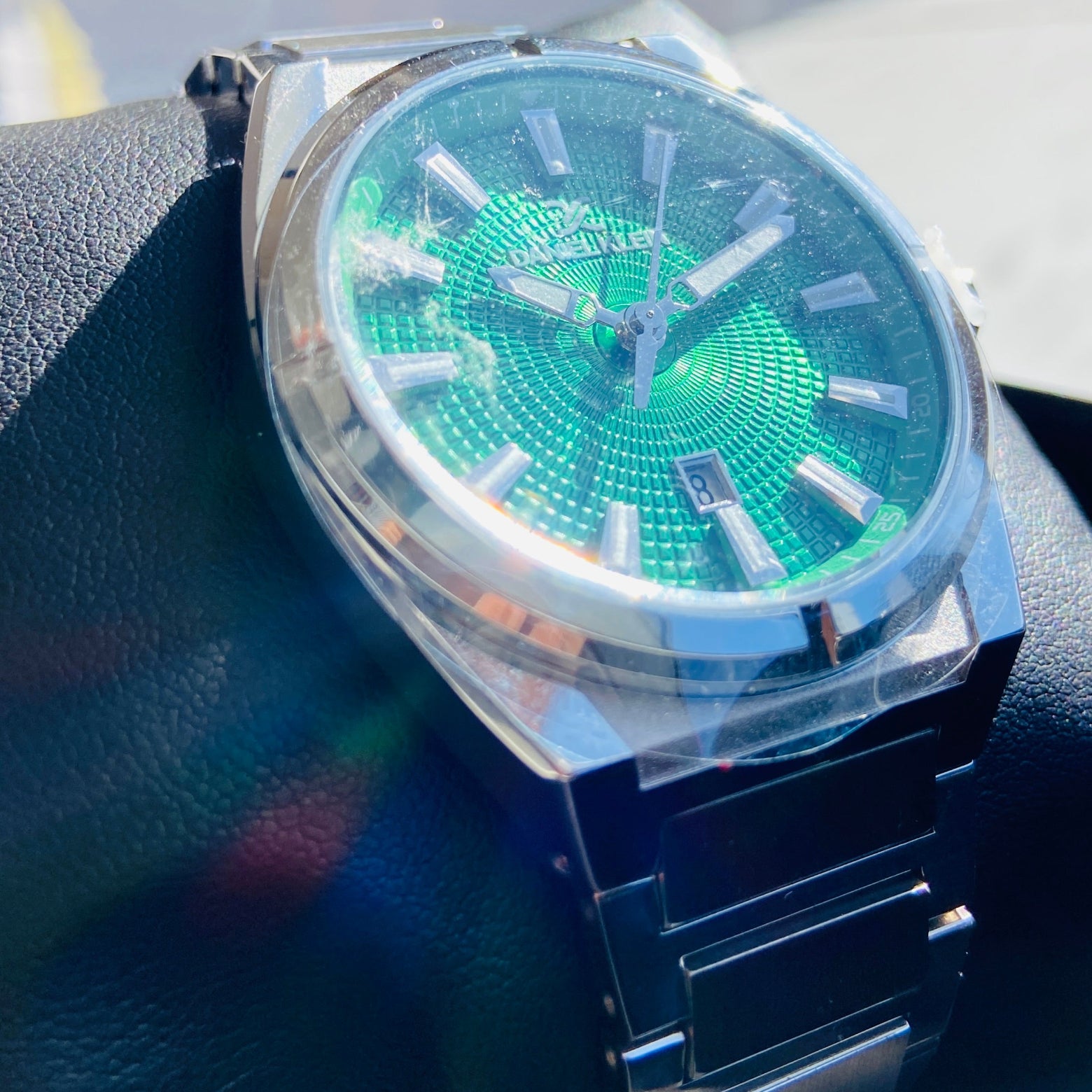 Green watch with silver case and band on a dark surface