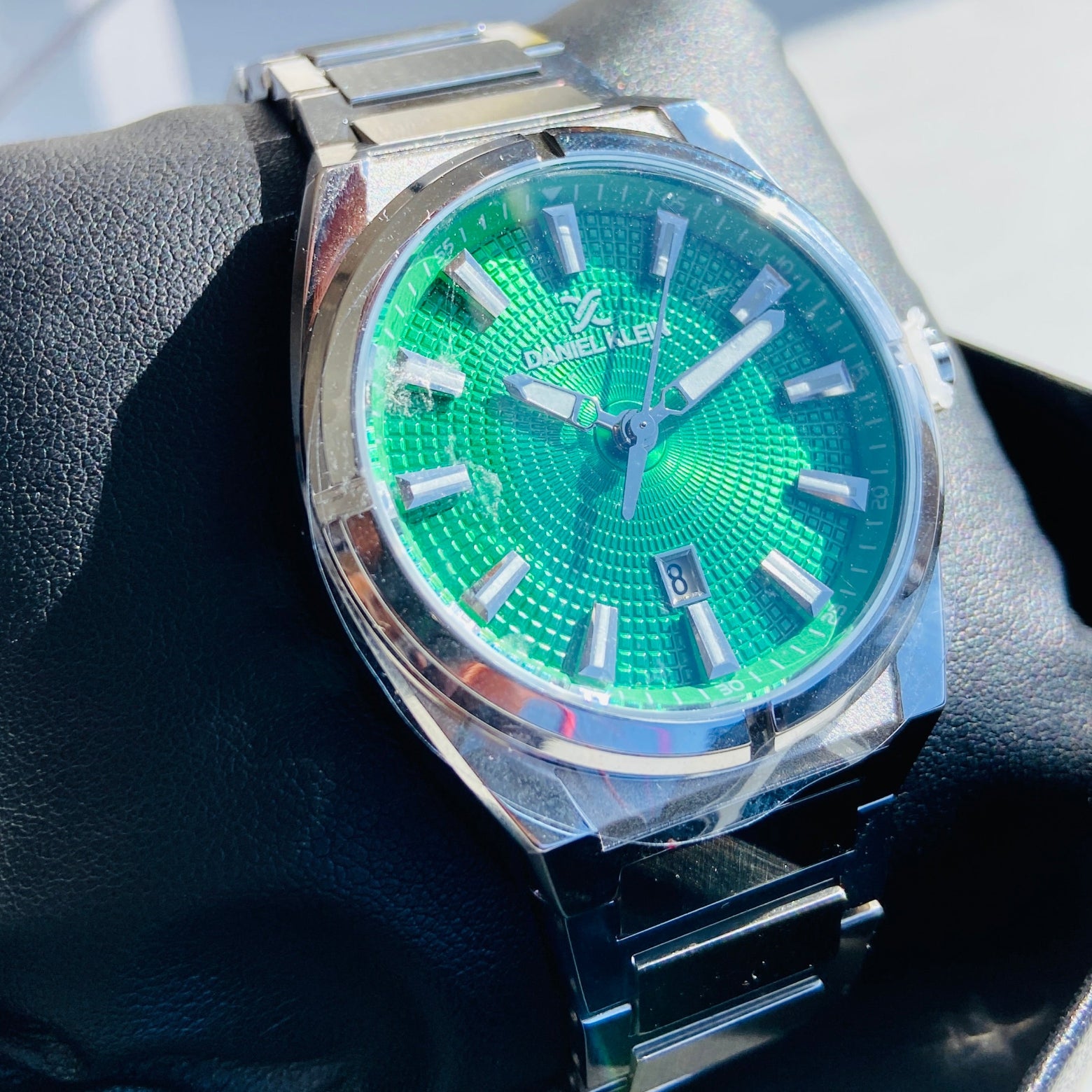 Silver watch with a green face on a dark surface