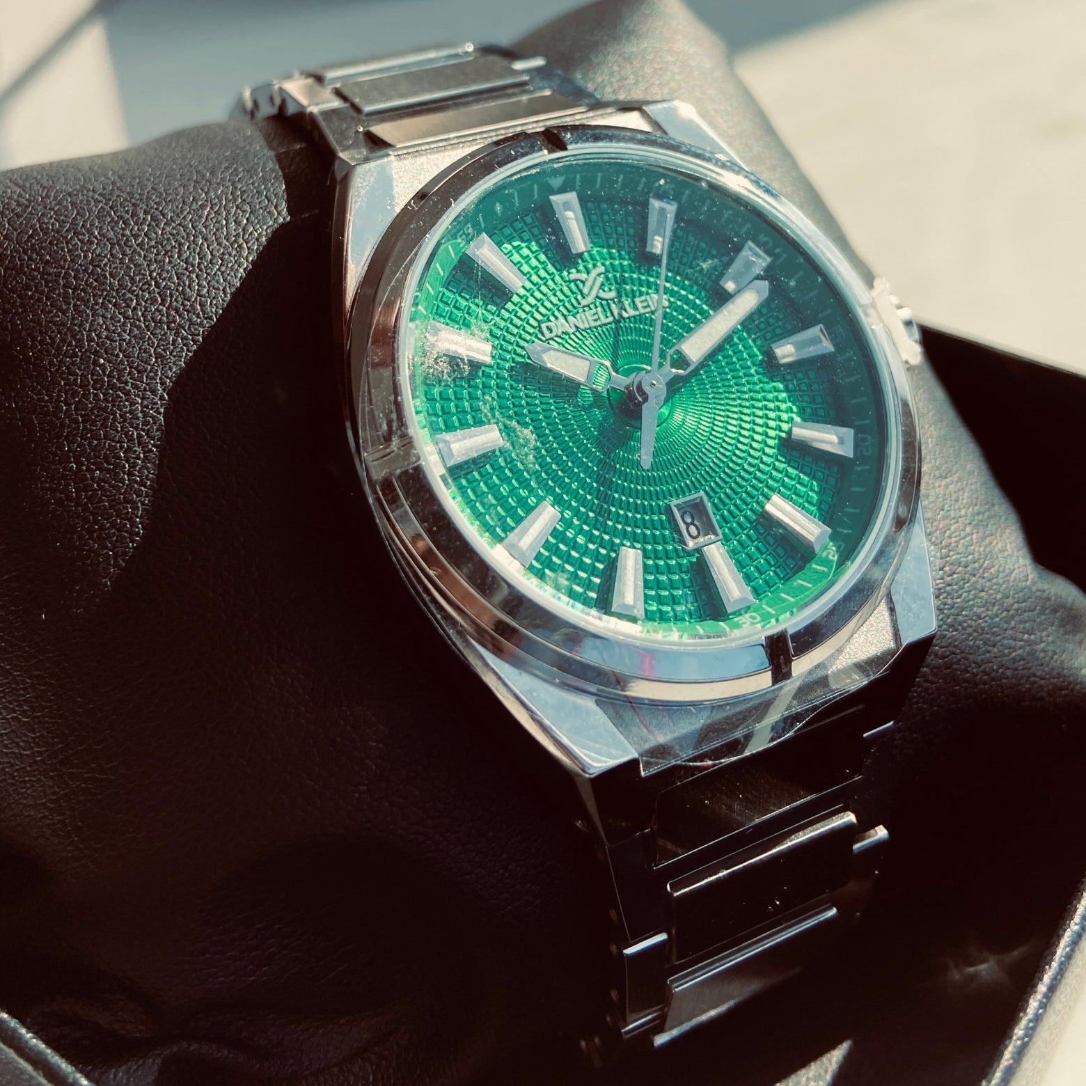 Luxury watch with green face and silver case on a black cushion