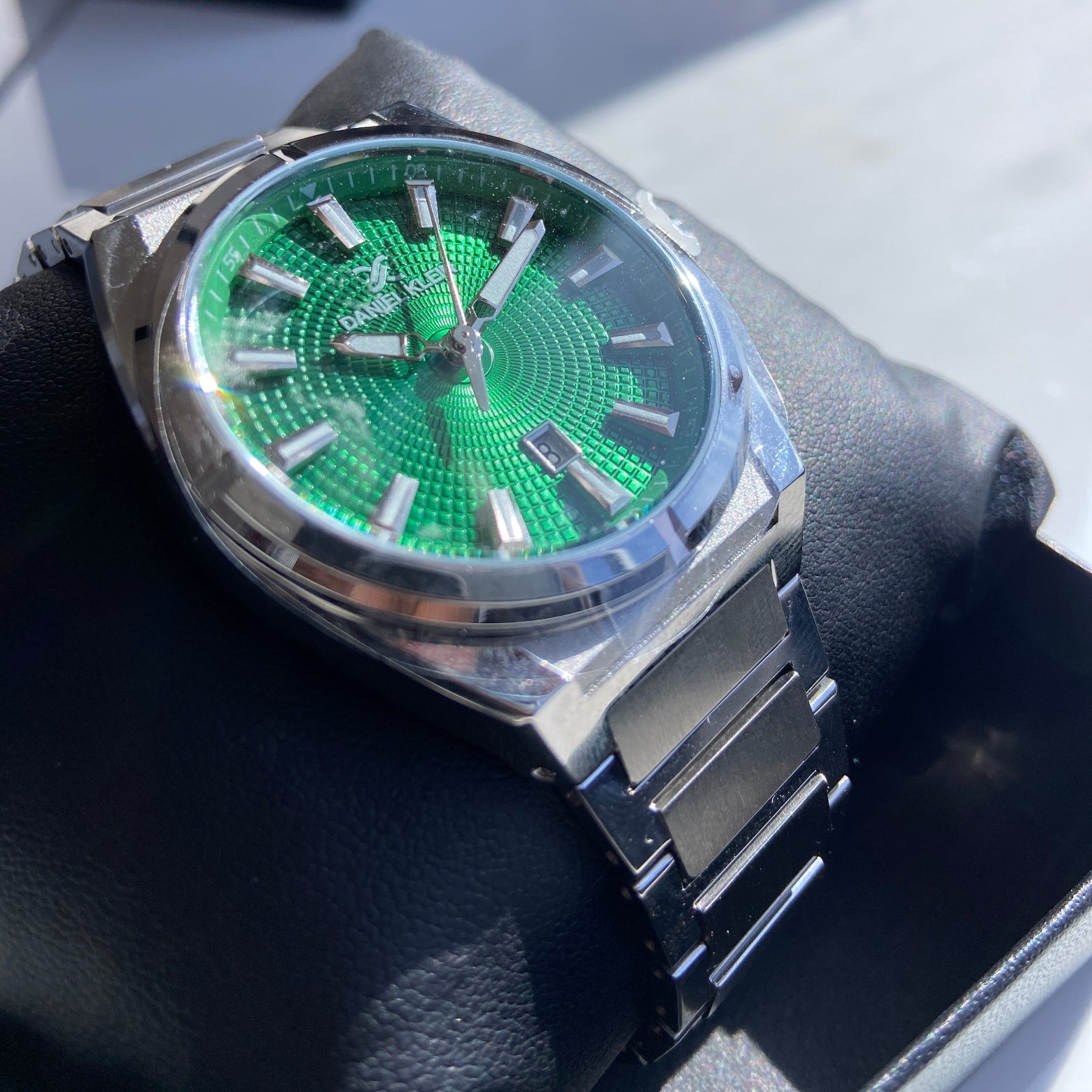 Wristwatch with a green face and silver case on a dark surface