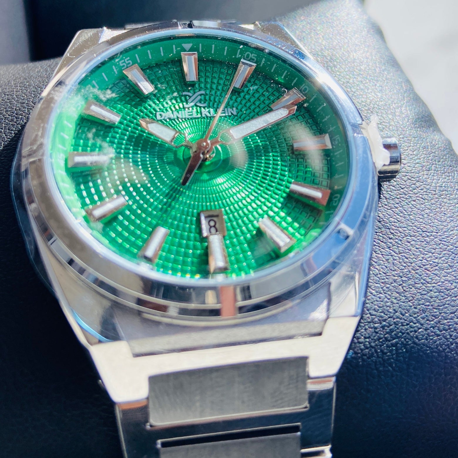 Silver watch with a green face on a dark surface