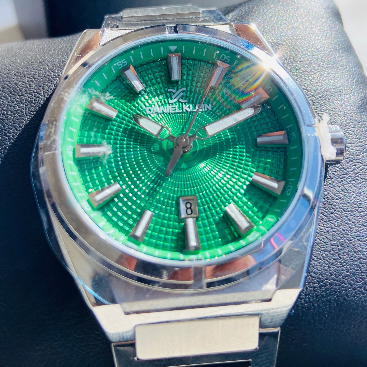 Watch with a green face and silver case on a dark surface