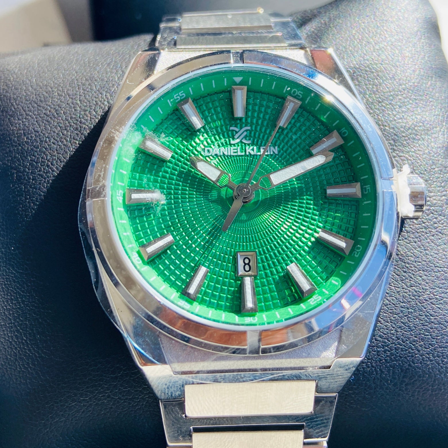 Green watch with silver case and band on a dark surface