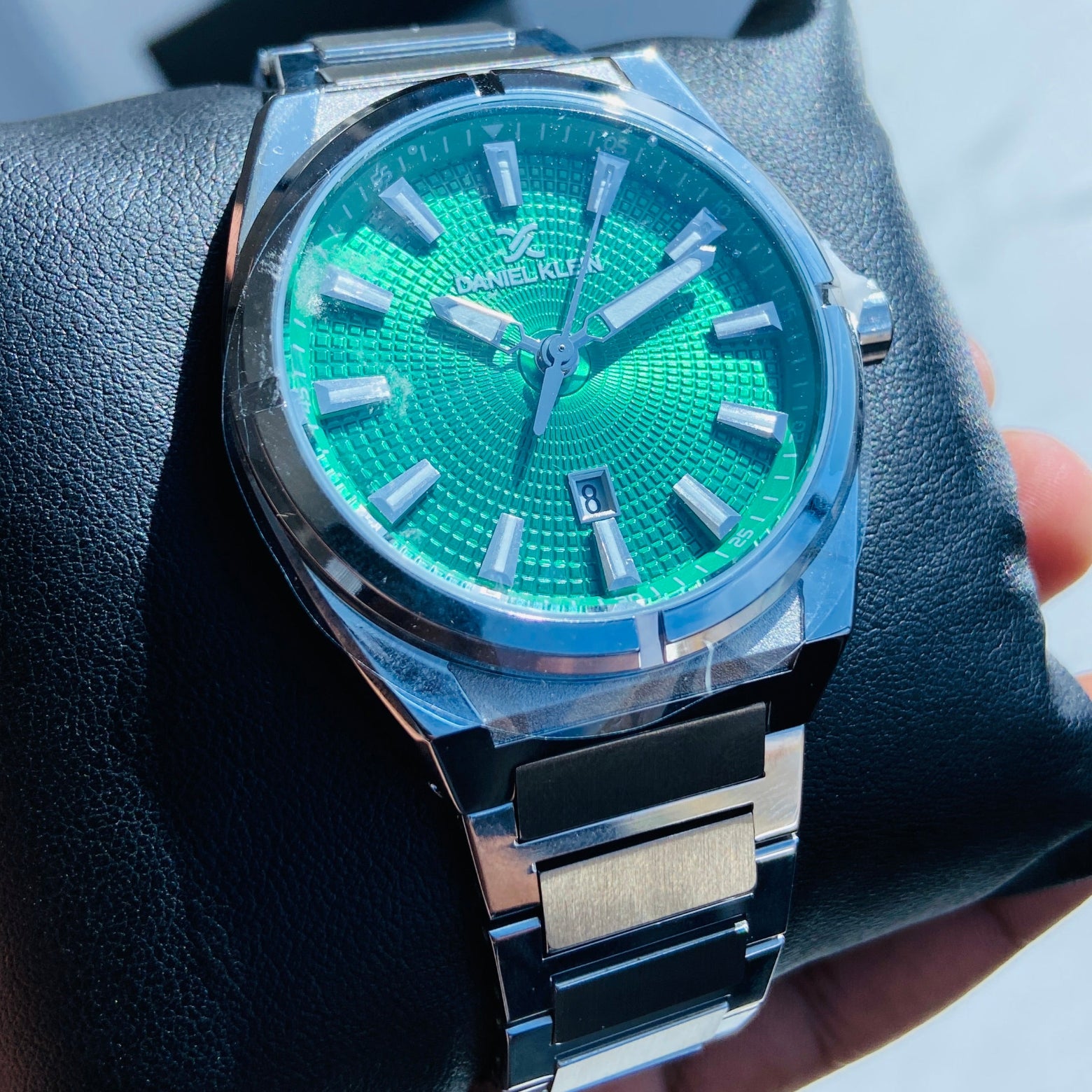 Green wristwatch with silver case held in a hand against a light background