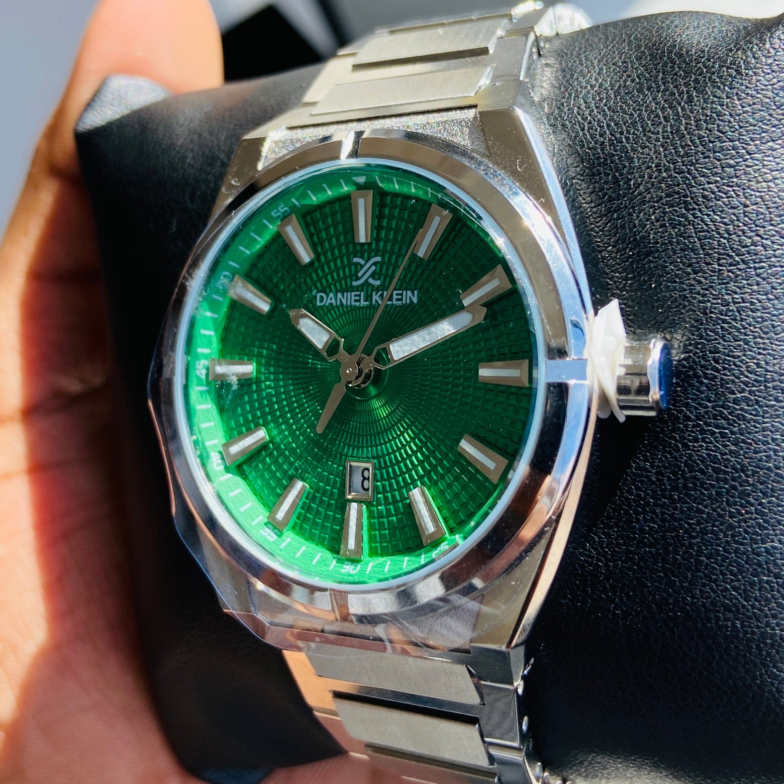 Watch with a green face and silver case held by a hand against a light background