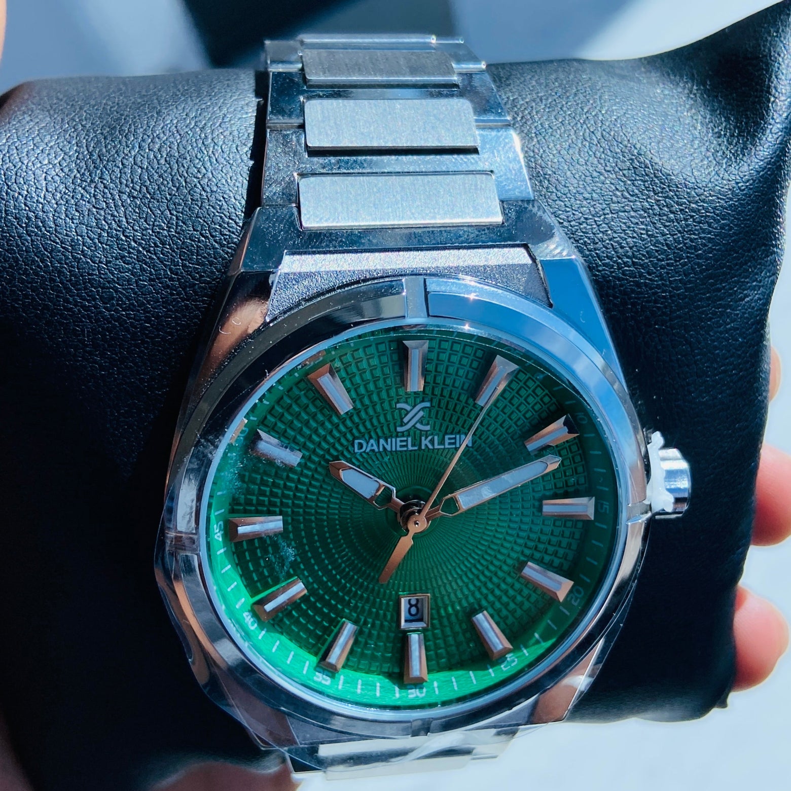 Hand holding a silver watch with a green face against a light background