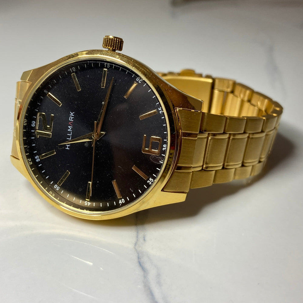 Gold watch with a black face on a white surface Gold wristwatch with black dial on a white cushion against a light background Gold Hallmark Watch watches mens kings DSJ Deep Shine Jewellers timeless timepiece time exclusive jewellery jewelry Your Time To Shine