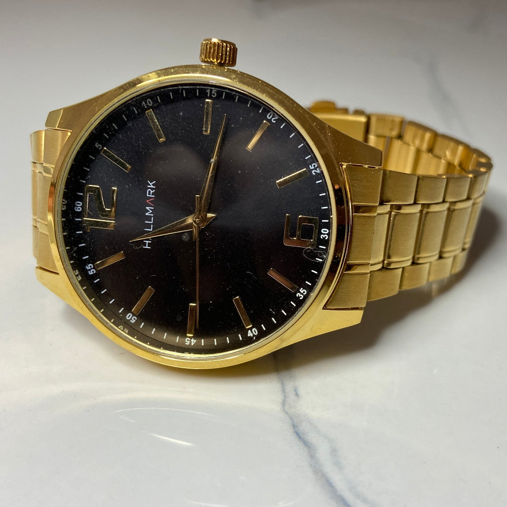 Gold watch with black face on a white surface Gold wristwatch with black dial on a white cushion against a light background Gold Hallmark Watch watches mens kings DSJ Deep Shine Jewellers timeless timepiece time exclusive jewellery jewelry Your Time To Shine