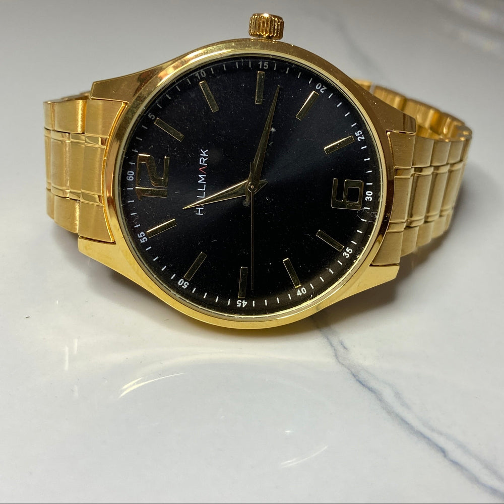 Gold watch with black face on a light gray surface Gold wristwatch with black dial on a white cushion against a light background Gold Hallmark Watch watches mens kings DSJ Deep Shine Jewellers timeless timepiece time exclusive jewellery jewelry Your Time To Shine