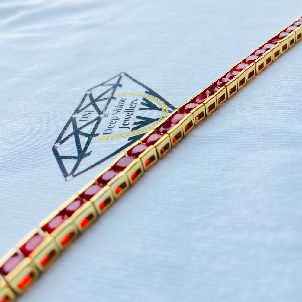 Gold bracelet with red stones on a light blue background with a jewelry brand logo. Gold bracelet with red gemstones on a white cushion Gold red ruby bracelet women queens ladies female tennis bracelet ruby red 925 silver sterling silver gold plated golden exclusive affordable luxury jewellery jewelry Deep Shine Jewellers DSJ Your Time To Shine trending best seller buy purchase bracelets 