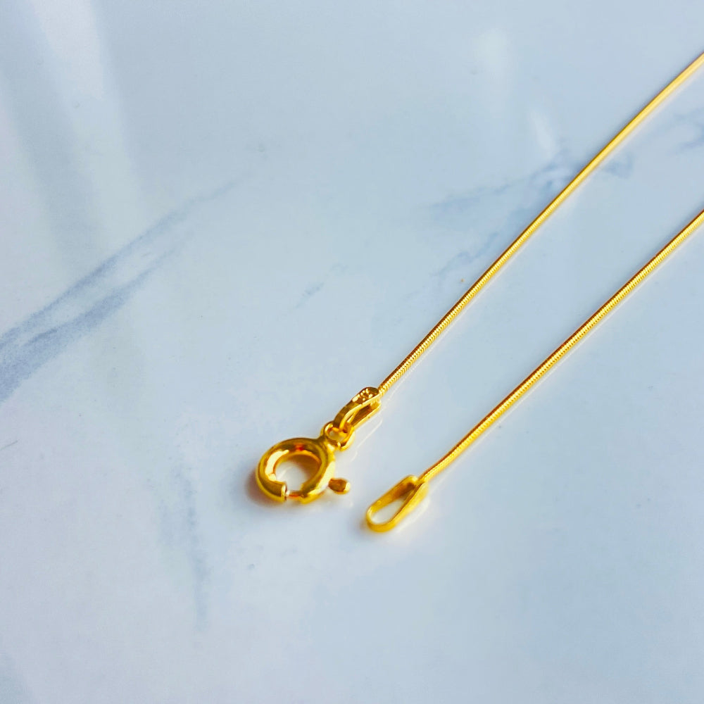 Gold necklace with a clasp on a light blue fabric background Gold bar on a light blue marble surface gold snake bone chain women men ladies gents kinds queens exclusive craftsmanship affordable luxury high quality premium jewellery jewelry Deep Shine Jewellers gold plated golden 925 silver sterling silver Your Time To Shine DSJ