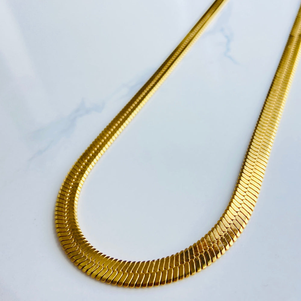 Gold necklace on a white marble surface gold herringbone chain ladies women queens affordable luxury stainless steel gold plated golden exclusive craftsmanship store Deep Shine Jewellers Jewellery jewelry trending best sellers DSJ Your Time To Shine radiant beauty