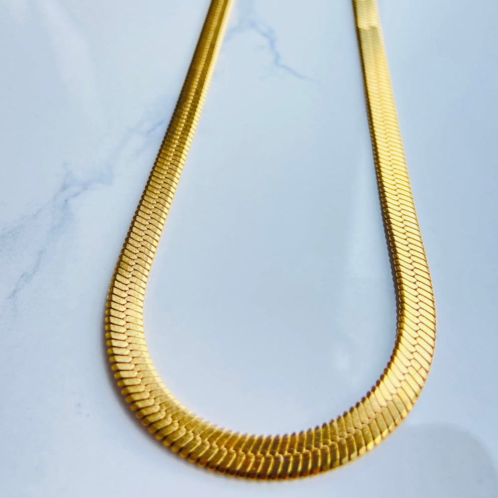 Gold necklace on a white marble surface gold herringbone chain ladies women queens affordable luxury stainless steel gold plated golden exclusive craftsmanship store Deep Shine Jewellers Jewellery jewelry trending best sellers DSJ Your Time To Shine radiant beauty