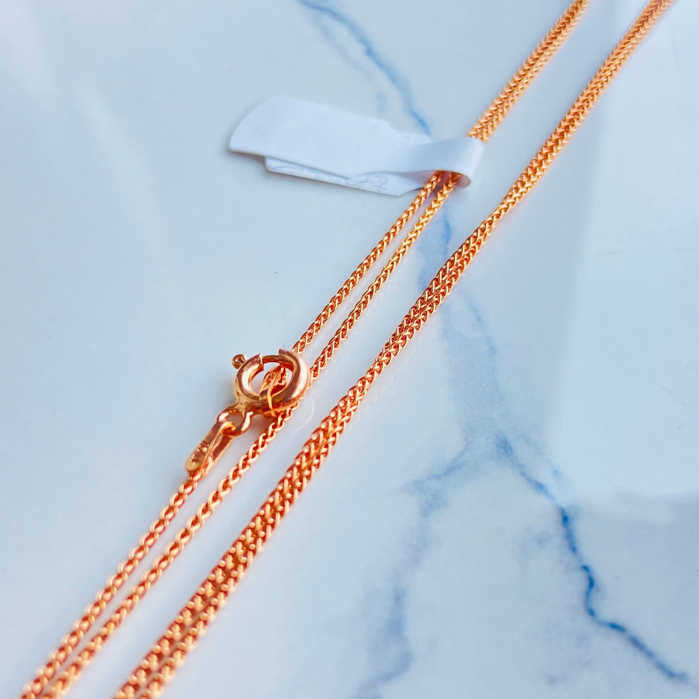 Gold chain necklace on a marble surface Rose gold necklace on a light blue marble surface rose gold wheat chain necklace women ladies queens 925 silver sterling silver rose gold plating roses premium jewellery jewelry affordable luxury elegant best seller trending Deep Shine Jewellers DSJ Your Time To Shine