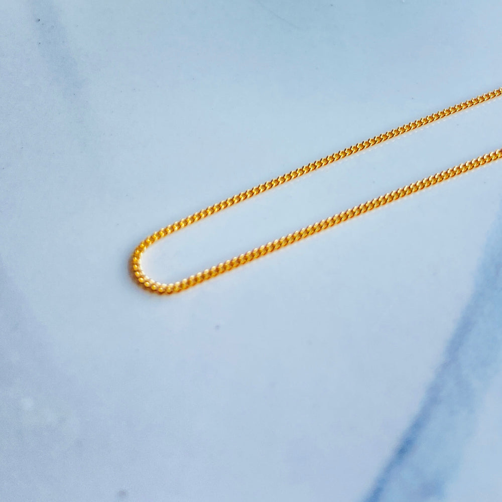 Gold chain on a light blue background gold micro flat curb chain necklace gold plated golden 925 silver sterling silver precious metals premium jewellery jewelry affordable luxury women mens gents ladies queens kings exclusive craftsmanship Deep Shine Jewellery DSJ Your Time To Shine trending best sellers kingdom