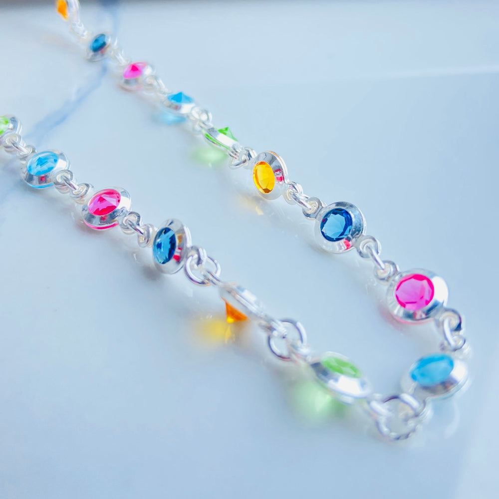 Colorful cross-shaped pendant on a dark surface Colourful Silver Cross Jewel Chain Exclusively by Deep Shine Jewellers. colourful gemstones diamonds lab diamonds sapphire pink yellow orange purple 925 silver sterling silver exclusive craftsmanship affordable luxury premium quality jewellery jewelry trending best sellers Your Time To Shine DSJ 