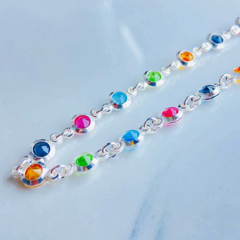 Colorful beaded necklace on a light blue background Colorful cross-shaped pendant on a dark surface Colourful Silver Cross Jewel Chain Exclusively by Deep Shine Jewellers. colourful gemstones diamonds lab diamonds sapphire pink yellow orange purple 925 silver sterling silver exclusive craftsmanship affordable luxury premium quality jewellery jewelry trending best sellers Your Time To Shine DSJ 