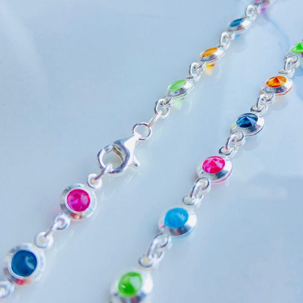 Colorful beaded necklace on a light blue marble surface Colorful cross-shaped pendant on a dark surface Colourful Silver Cross Jewel Chain Exclusively by Deep Shine Jewellers. colourful gemstones diamonds lab diamonds sapphire pink yellow orange purple 925 silver sterling silver exclusive craftsmanship affordable luxury premium quality jewellery jewelry trending best sellers Your Time To Shine DSJ 