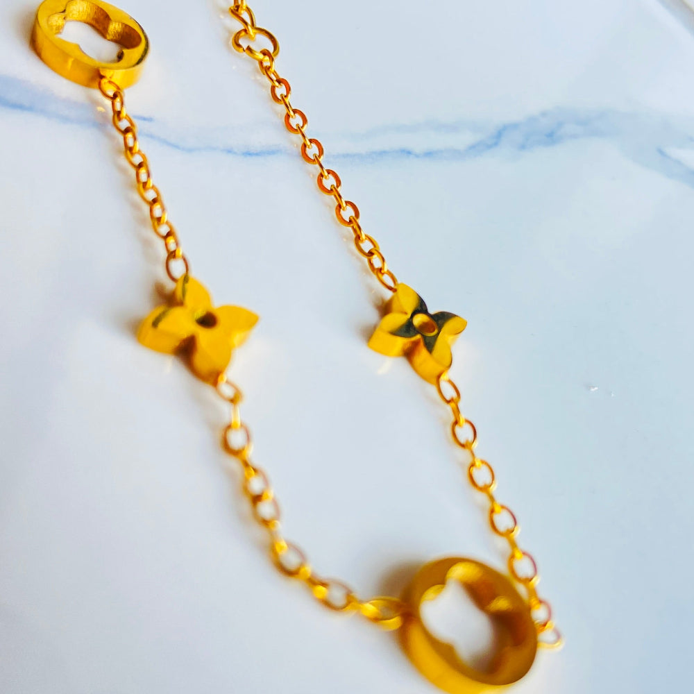 Gold necklace with geometric pendants on a light background Gold bracelet with clover-shaped charms on a light blue background gold clover bracelet womens mens ladies gents queens kings van cleef and arpels charm gold plated golden premium jewellery jewelry exclusive craftsmanship cape town best sellers stainless steel trending modern classy Deep Shine Jewellers DSJ Your Time To Shine online store affordable luxury 