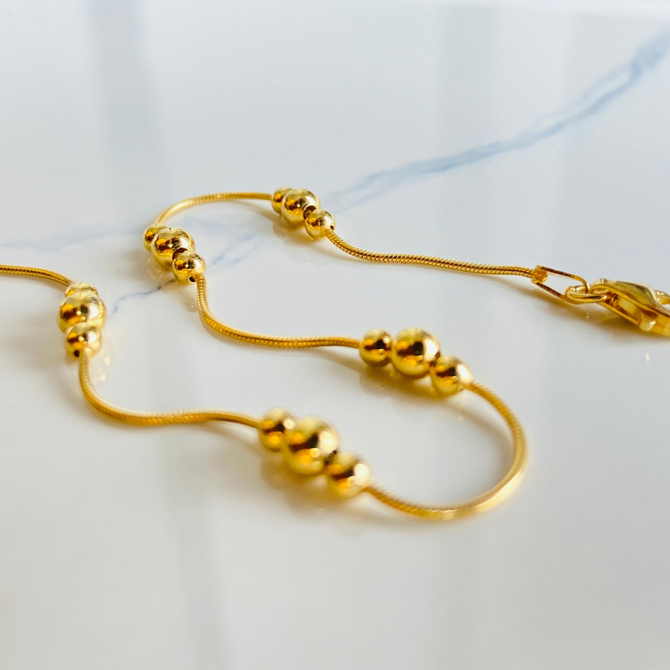 Gold necklace on a white surface Gold beaded necklace on a light blue background gold ball and snake bracelet women ladies queens gold plated golden 925 silver sterling silver exclusive craftsmanship affordable luxury premium quality jewellery jewelry Deep Shine Jewellery DSJ Your Time To Shine best sellers trending chrismas sale gifts 