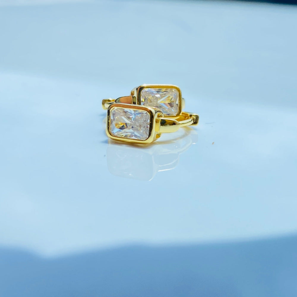 Gold ring with a clear gemstone on a white surface with blue background Gold hoop earring with clear stones on a reflective surface with blue sky background gold single stone sleeper earrings women ladies queens gold plated golden cubic zirconia diamond baguette 925 silver sterling silver exclusive craftsmanship high quality premium affordable luxury Deep Shine Jewellers jewellery jewelry Your Time To Shine DSJ