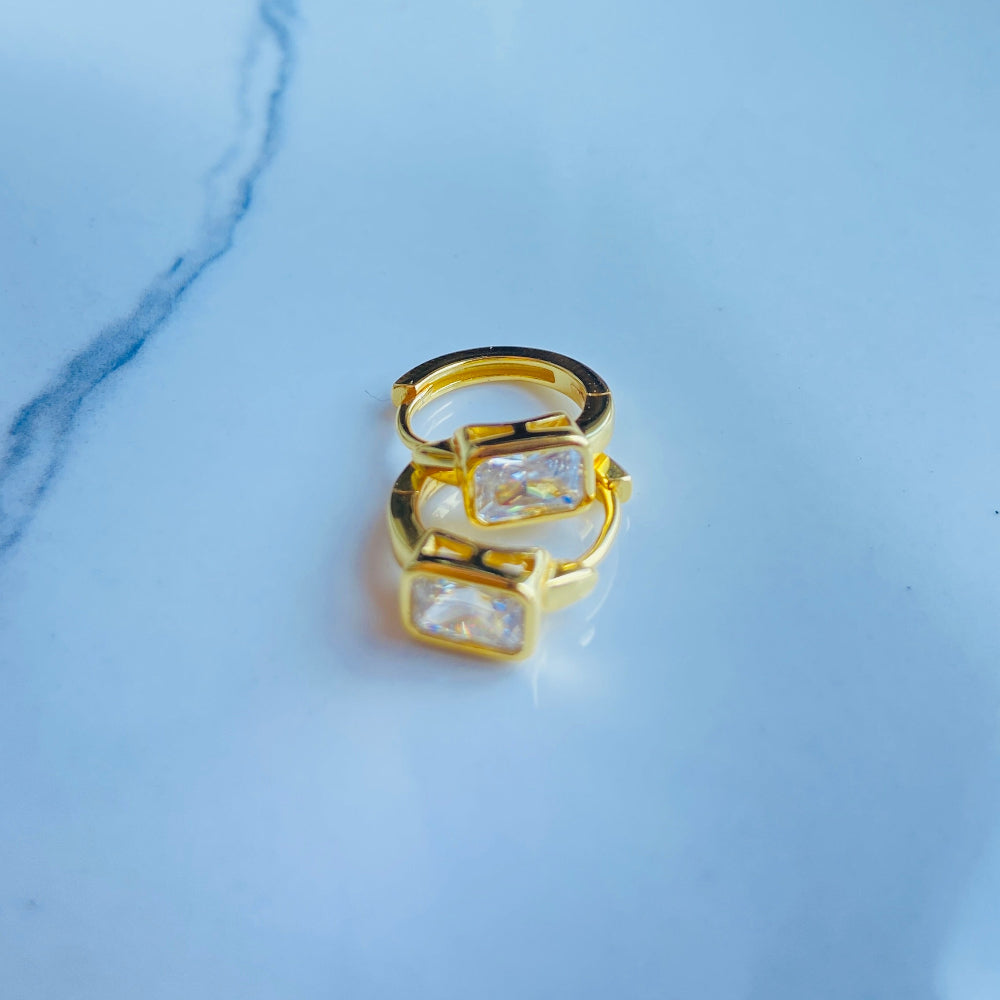 Gold ring with clear gemstones on a light blue marble background Gold hoop earring with clear stones on a reflective surface with blue sky background gold single stone sleeper earrings women ladies queens gold plated golden cubic zirconia diamond baguette 925 silver sterling silver exclusive craftsmanship high quality premium affordable luxury Deep Shine Jewellers jewellery jewelry Your Time To Shine DSJ