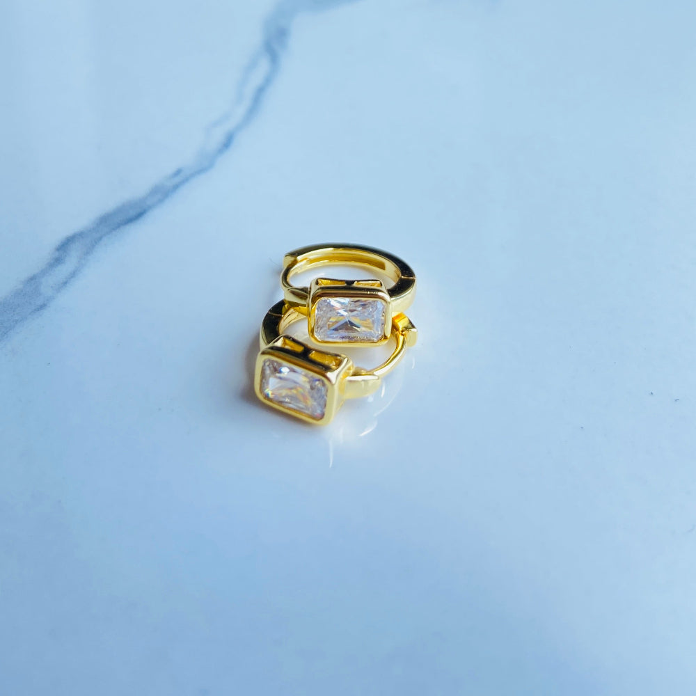 Gold ring with a clear gemstone on a marble surface Gold hoop earring with clear stones on a reflective surface with blue sky background gold single stone sleeper earrings women ladies queens gold plated golden cubic zirconia diamond baguette 925 silver sterling silver exclusive craftsmanship high quality premium affordable luxury Deep Shine Jewellers jewellery jewelry Your Time To Shine DSJ