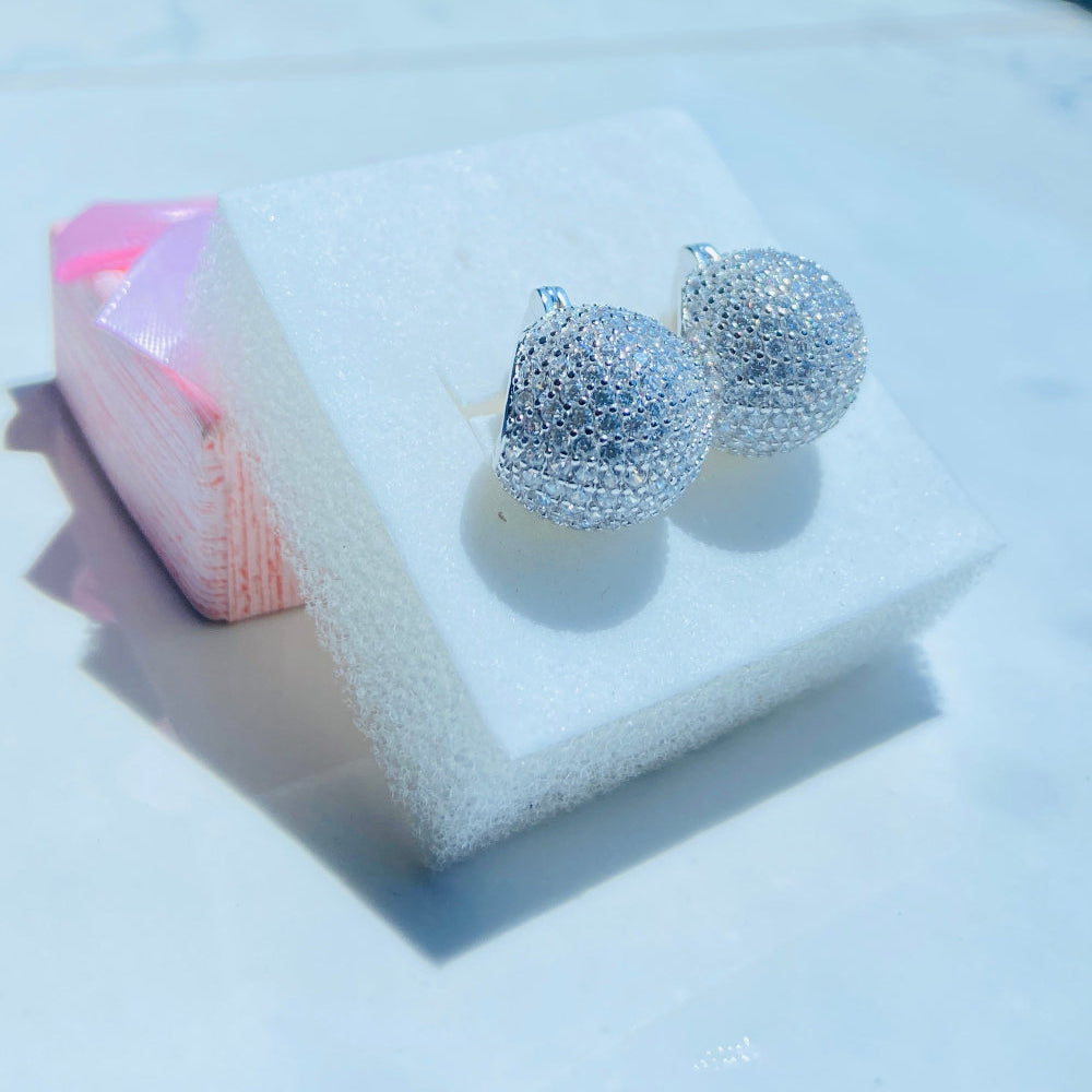 Silver glittery earrings on a white stand with a blurred outdoor background Silver earrings on a white stand with a blurred outdoor background silver ice dome earrings women ladies queens 925 silver sterling silver cubic zirconia diamonds lab diamonds affordable luxury exclusive craftsmanship Deep Shine Jewellers jewellery jewelry DSJ Your Time To Shine limited premium jewellery trending