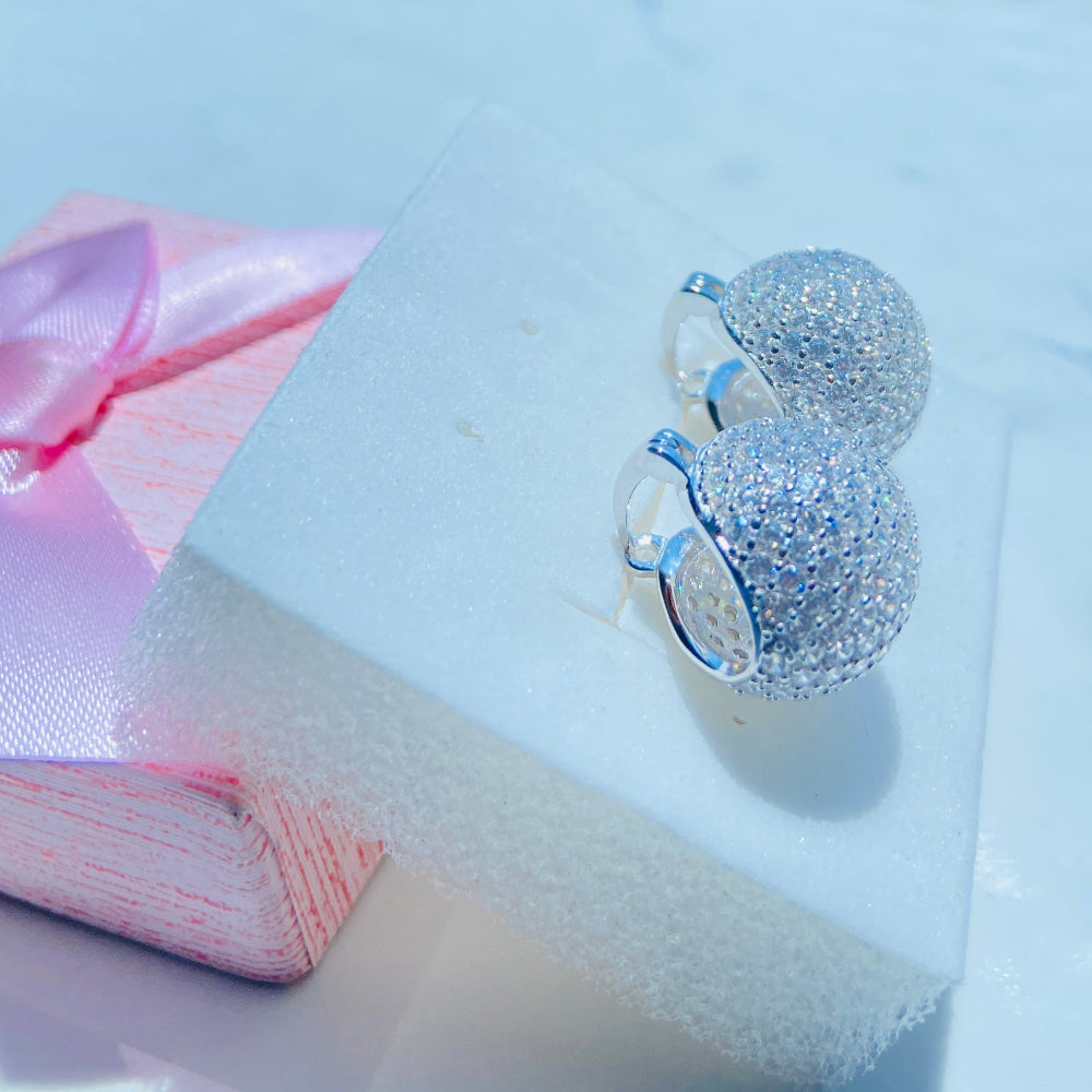 Silver glittery ring on a pink fabric with a blurred outdoor background Silver earrings on a white stand with a blurred outdoor background silver ice dome earrings women ladies queens 925 silver sterling silver cubic zirconia diamonds lab diamonds affordable luxury exclusive craftsmanship Deep Shine Jewellers jewellery jewelry DSJ Your Time To Shine limited premium jewellery trending