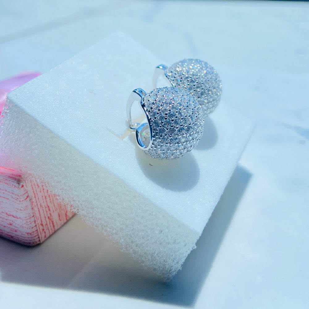 Silver heart-shaped earrings on a white stand with a blurred outdoor background Silver earrings on a white stand with a blurred outdoor background silver ice dome earrings women ladies queens 925 silver sterling silver cubic zirconia diamonds lab diamonds affordable luxury exclusive craftsmanship Deep Shine Jewellers jewellery jewelry DSJ Your Time To Shine limited premium jewellery trending