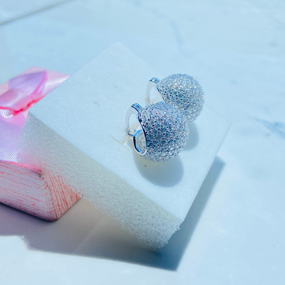 Silver glittery earrings on a white surface with a blurred background Silver earrings on a white stand with a blurred outdoor background silver ice dome earrings women ladies queens 925 silver sterling silver cubic zirconia diamonds lab diamonds affordable luxury exclusive craftsmanship Deep Shine Jewellers jewellery jewelry DSJ Your Time To Shine limited premium jewellery trending