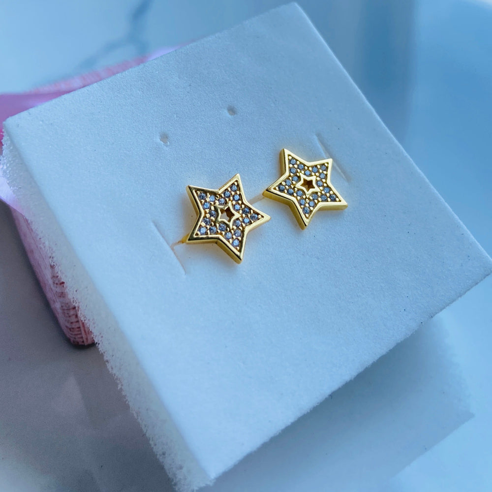 Gold star-shaped earrings on a white stand with a blurred background Gold star-shaped earrings on a white box with a scenic background gold iced star stud earring women men ladies gents kings queens 925 silver sterling silver gold plated golden shine exclusive craftsmanship Deep Shine Jewellers Jewellery jewelry trending shop now store bright beauty 
