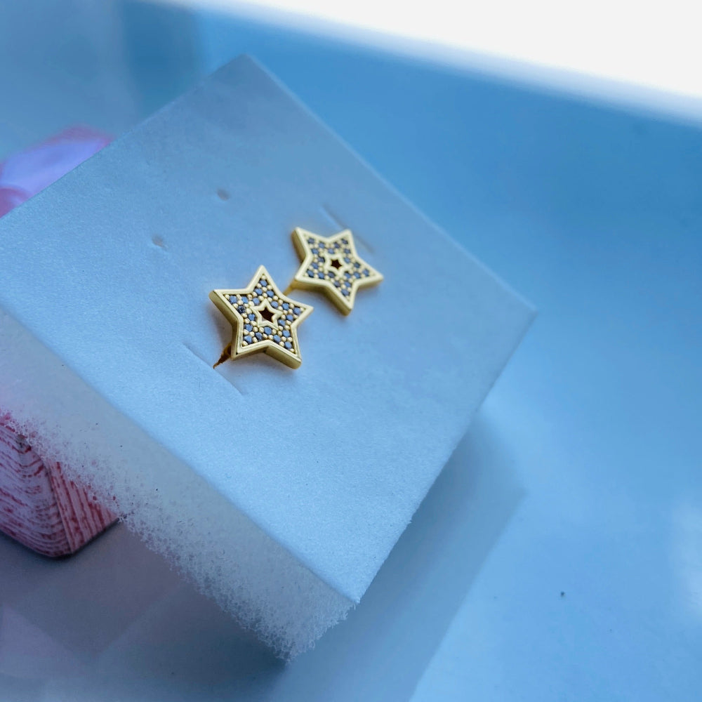 Gold star-shaped earrings on a clear stand with a blurred background Gold star-shaped earrings on a white box with a scenic background gold iced star stud earring women men ladies gents kings queens 925 silver sterling silver gold plated golden shine exclusive craftsmanship Deep Shine Jewellers Jewellery jewelry trending shop now store bright beauty 