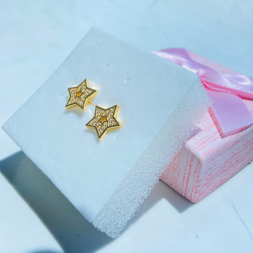 Gold star-shaped earrings on a light blue cushion with a blurred outdoor background Gold star-shaped earrings on a white box with a scenic background gold iced star stud earring women men ladies gents kings queens 925 silver sterling silver gold plated golden shine exclusive craftsmanship Deep Shine Jewellers Jewellery jewelry trending shop now store bright beauty 