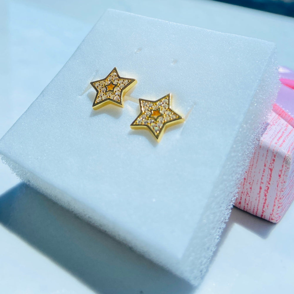 Gold star-shaped earrings on a white box with a scenic background gold iced star stud earring women men ladies gents kings queens 925 silver sterling silver gold plated golden shine exclusive craftsmanship Deep Shine Jewellers Jewellery jewelry trending shop now store bright beauty 