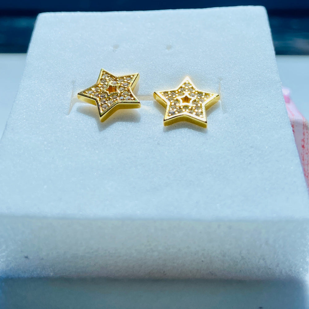 Gold star-shaped earrings on a white box with a scenic background gold iced star stud earring women men ladies gents kings queens 925 silver sterling silver gold plated golden shine exclusive craftsmanship Deep Shine Jewellers Jewellery jewelry trending shop now store bright beauty 