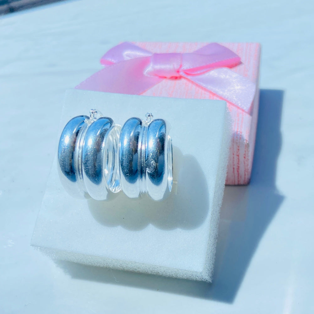 Silver ring with blue stones on a white stand, with a pink box featuring a bow in the background.Silver spiral earring on a white stand with a blurred background silver double hoop earrings women ladies queens 925 silver sterling silver exclusive affordable luxury jewellery jewelry Deep Shine Jewellers trending style accessories Your Time To Shine gift christmas DSJ 