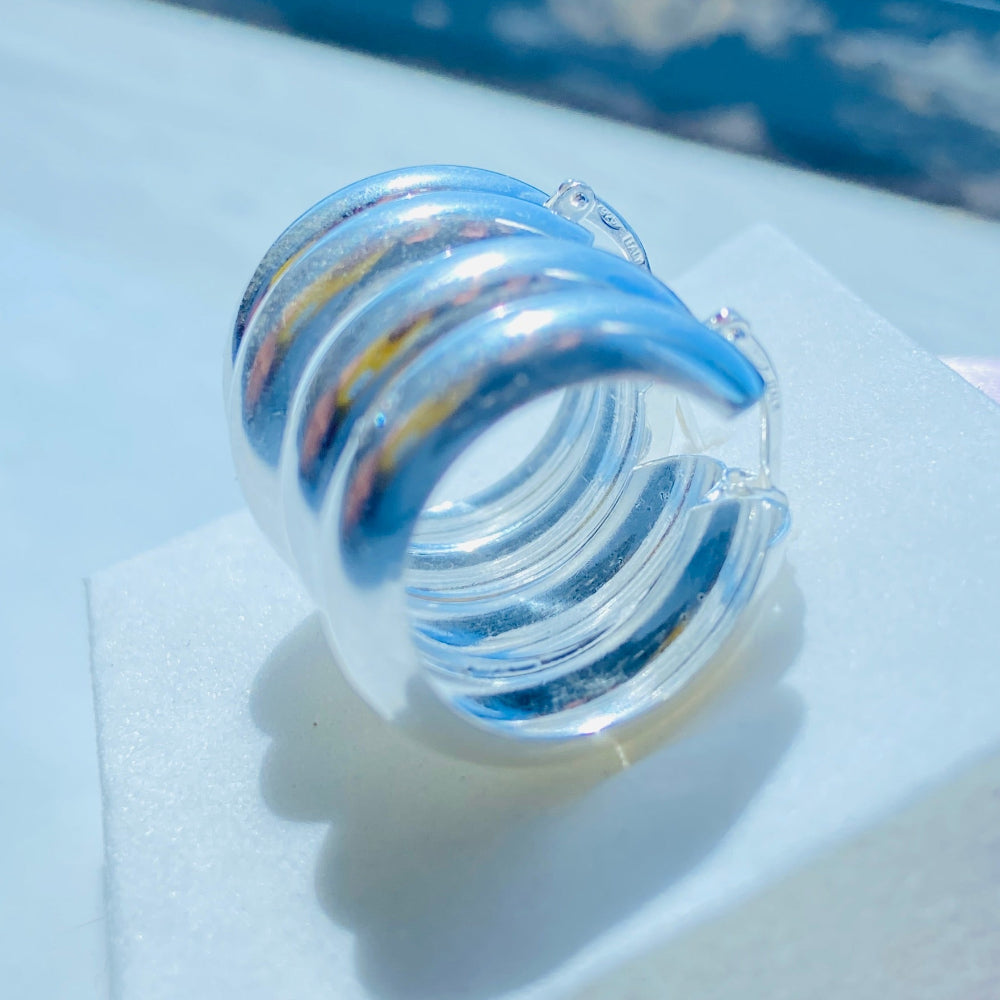 Clear glass spiral object on a white surface with a blue background Silver spiral earring on a white stand with a blurred background silver double hoop earrings women ladies queens 925 silver sterling silver exclusive affordable luxury jewellery jewelry Deep Shine Jewellers trending style accessories Your Time To Shine gift christmas DSJ 