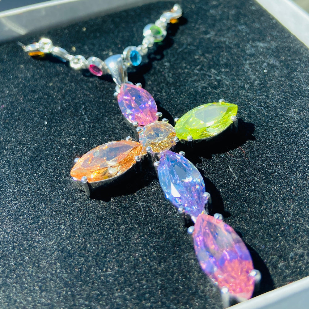 Colorful beaded cross on a dark surface with a blurred outdoor background Colorful cross-shaped pendant on a dark surface Colourful Silver Cross Jewel Chain Exclusively by Deep Shine Jewellers. colourful gemstones diamonds lab diamonds sapphire pink yellow orange purple 925 silver sterling silver exclusive craftsmanship affordable luxury premium quality jewellery jewelry trending best sellers Your Time To Shine DSJ 