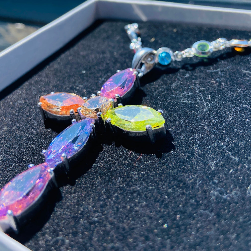Colorful butterfly-shaped necklace on a black surface with a blurred outdoor background Colorful cross-shaped pendant on a dark surface Colourful Silver Cross Jewel Chain Exclusively by Deep Shine Jewellers. colourful gemstones diamonds lab diamonds sapphire pink yellow orange purple 925 silver sterling silver exclusive craftsmanship affordable luxury premium quality jewellery jewelry trending best sellers Your Time To Shine DSJ 
