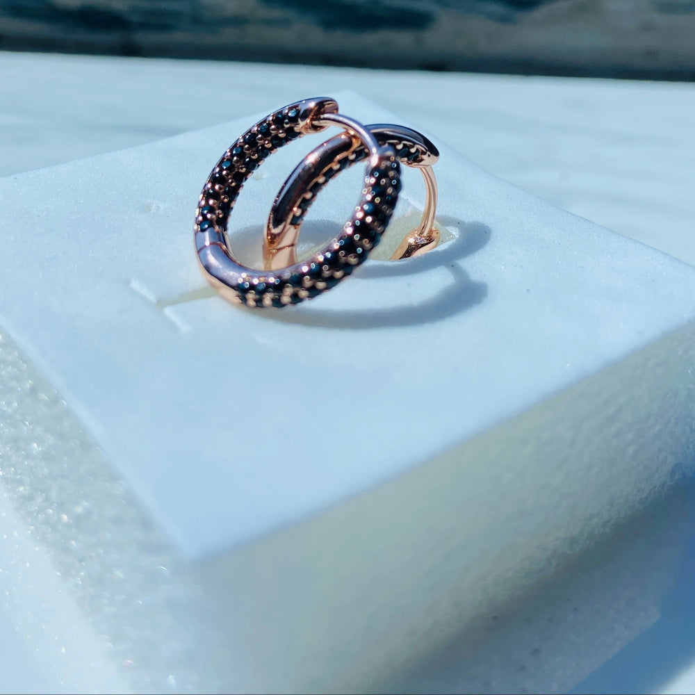 Rose gold ring with embedded gemstones on a white stand against a blue background Rose gold ring with black gemstones on a white box against a blue window background rose gold flooded sleeper hoop earrings for women ladies queens black stones black diamond cubic zirconia lab diamond 925 silver sterling silver exclusive Deep Shine Jewellers jewellery jewelry Your Time To Shine DSJ