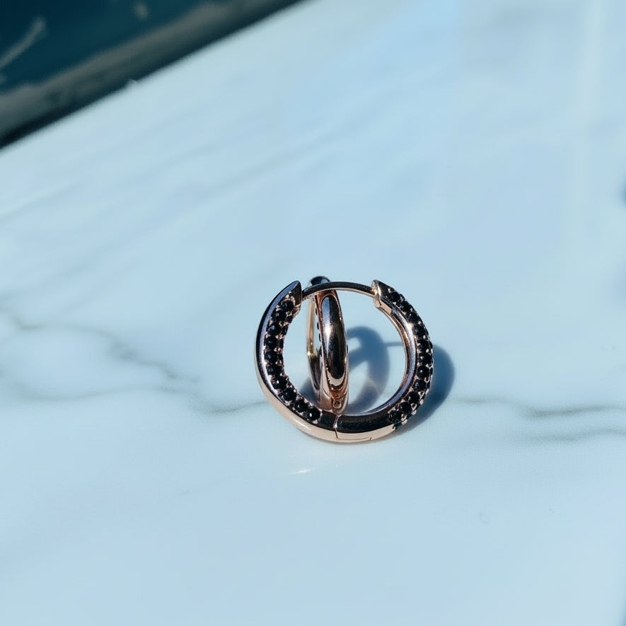 Rose gold hoop earrings on a clear stand with a blurred background Rose gold ring with black gemstones on a white box against a blue window background rose gold flooded sleeper hoop earrings for women ladies queens black stones black diamond cubic zirconia lab diamond 925 silver sterling silver exclusive Deep Shine Jewellers jewellery jewelry Your Time To Shine DSJ