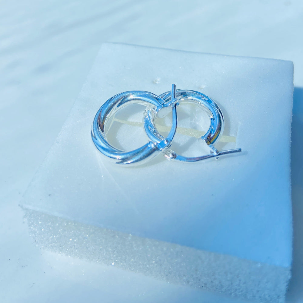 Silver hoop earrings on a light blue fabric background Silver hoop earrings on a white square platform with a blue background silver twist sleeper hoop earrings for women womens ladies queen 925 silver sterling silver affordable luxury jewellery jewelry trendy fashion Deep Shine Jewellers shop now DSJ 