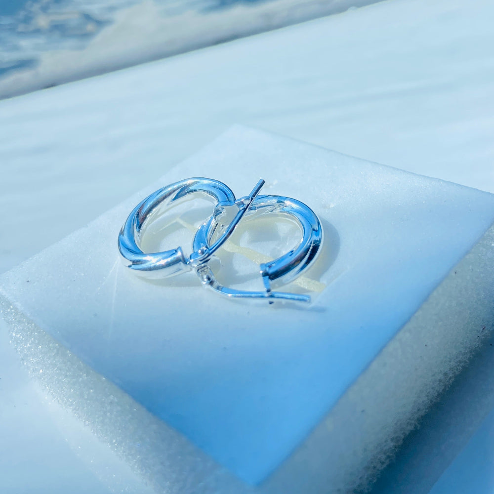 Silver hoop earrings on a light blue cushion with a blurred outdoor background Silver hoop earrings on a white square platform with a blue background silver twist sleeper hoop earrings for women womens ladies queen 925 silver sterling silver affordable luxury jewellery jewelry trendy fashion Deep Shine Jewellers shop now DSJ 