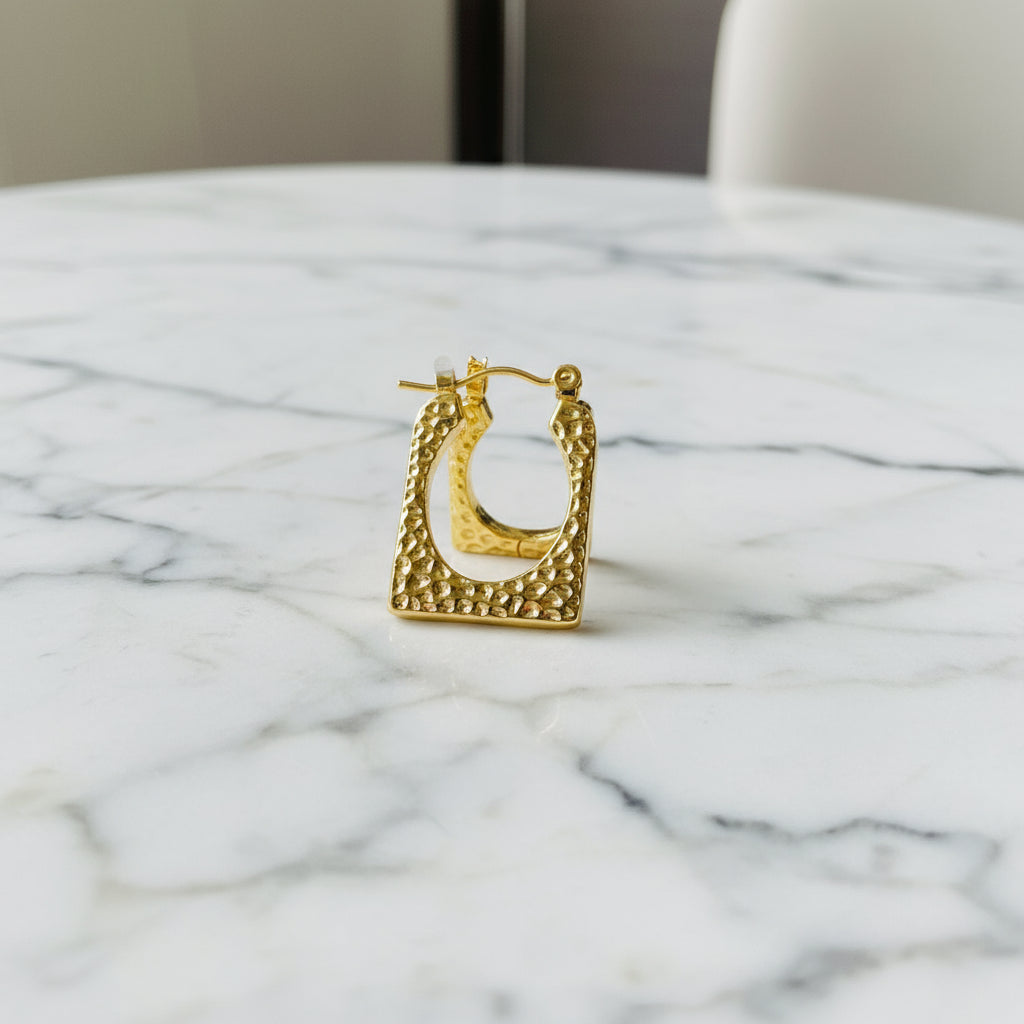 Gold ring with intricate design on a white cushion against a blue background Gold hoop earrings on a light blue surface gold detailed rectangle earrings exclusive by Deep Shine Jewellers jewellery jewelry DSJ Your Time To Shine golden shine