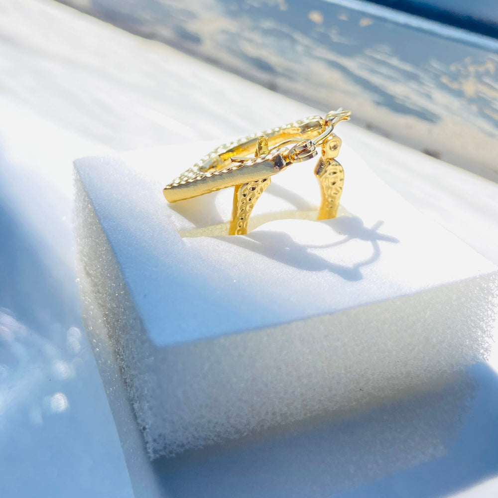 Gold ring with gemstones on a white cushion against a blue background Gold hoop earrings on a light blue surface gold detailed rectangle earrings exclusive by Deep Shine Jewellers jewellery jewelry DSJ Your Time To Shine golden shine