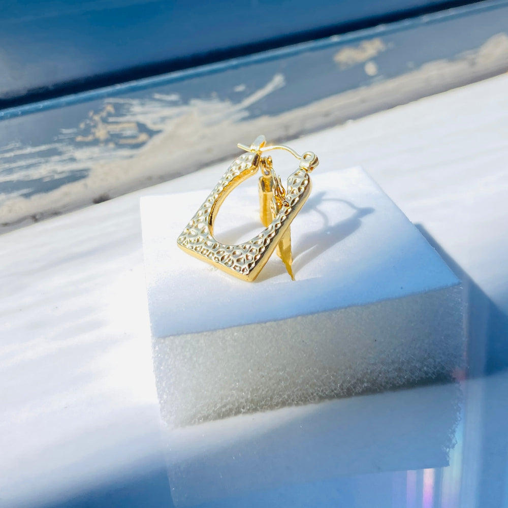 Gold hoop earring on a white stand with a scenic window view in the background Gold hoop earrings on a light blue surface gold detailed rectangle earrings exclusive by Deep Shine Jewellers jewellery jewelry DSJ Your Time To Shine golden shine