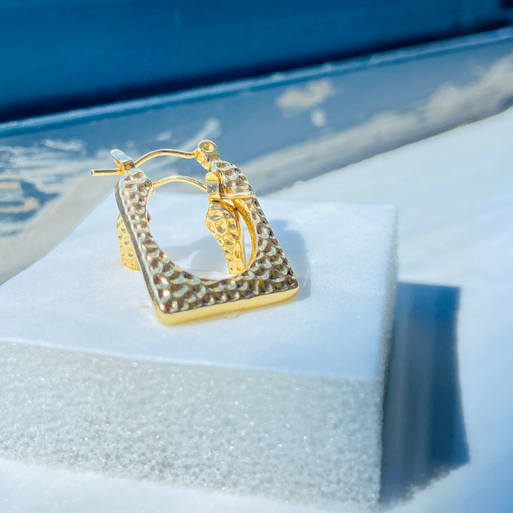 Gold hoop earrings on a white cushion with a blue background Gold hoop earrings on a light blue surface gold detailed rectangle earrings exclusive by Deep Shine Jewellers jewellery jewelry DSJ Your Time To Shine golden shine