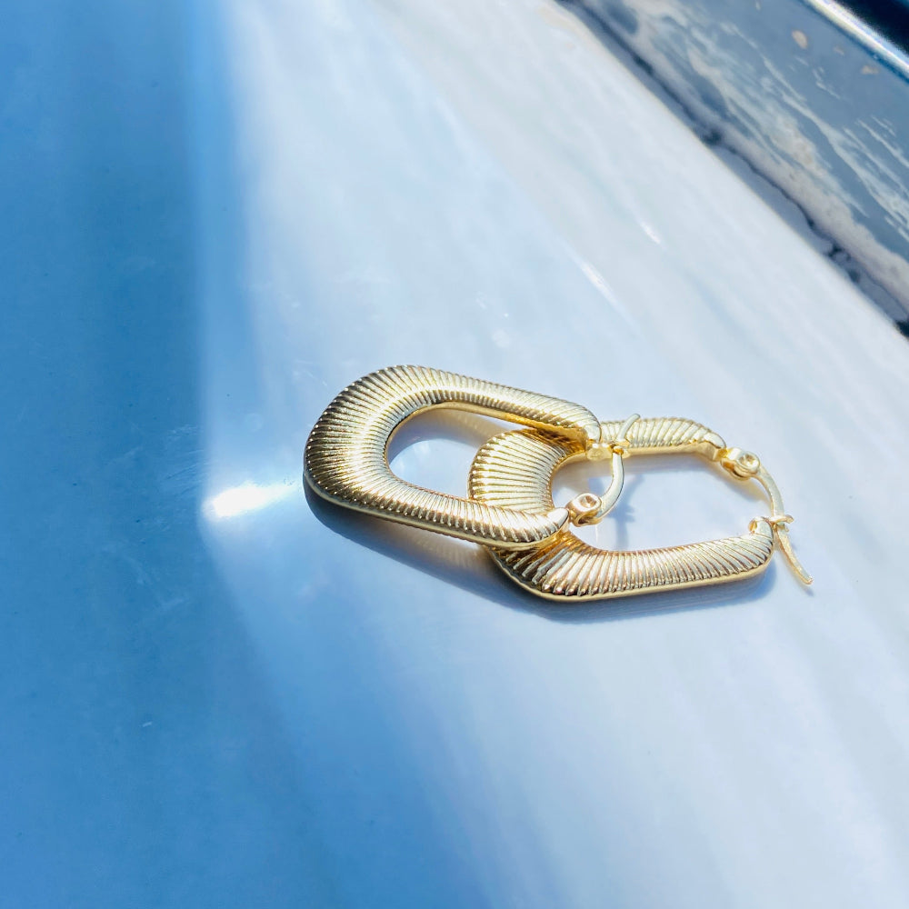 Gold hoop earrings on a light blue surface with a blurred natural background Gold striped rectangle earrings jewellery jewelry Deep Shine Jewellers stainless steel gold-plated affordable luxury DSJ Your Time To Shine exclusive radiant womens lady's queens kingdom