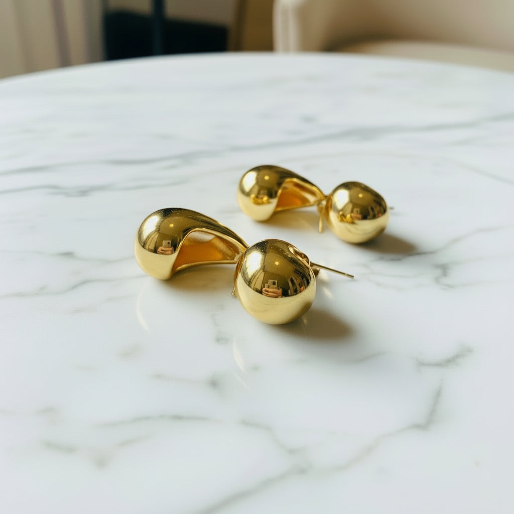 Gold sunglasses on a pink stand with a blurred outdoor background Gold Drop Form Earrings stainless steel female womens queens jewellery jewelry Deep Shine Jewellers Your Time To Shine DSJ affordable luxury exclusive craftsmanship